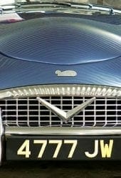 Front view of a vintage blue sports car with the license plate "4777 jw," ideal for storing in self storage, featuring prominent headlights and a chrome grille.