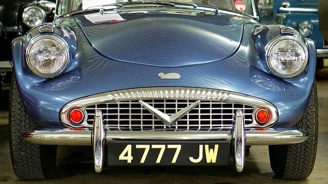 Front view of a vintage blue sports car with the license plate "4777 jw," ideal for storing in self storage, featuring prominent headlights and a chrome grille.